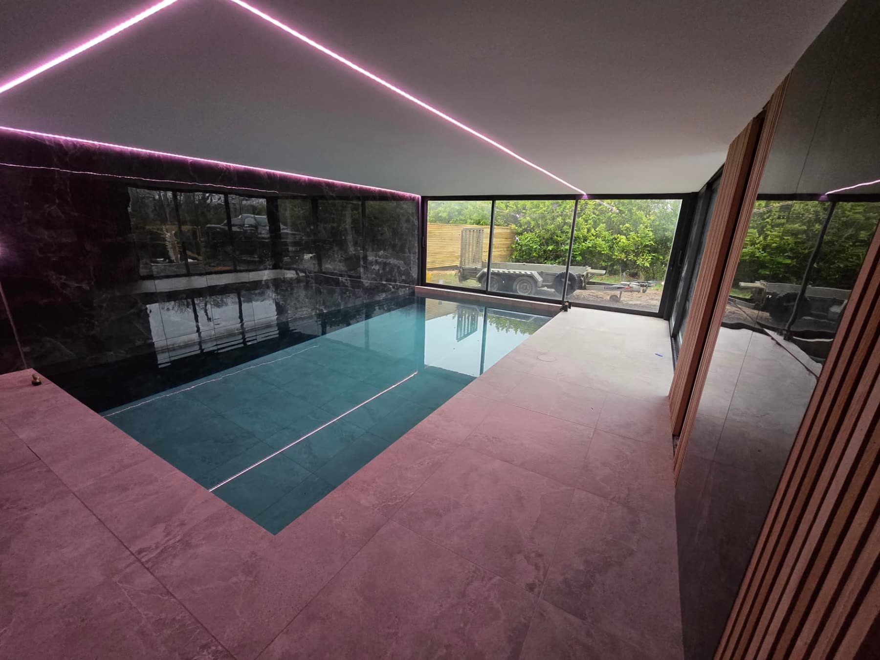 Indoor swimming pool with black tiled walls, ambient lighting and glazed doors to the garden