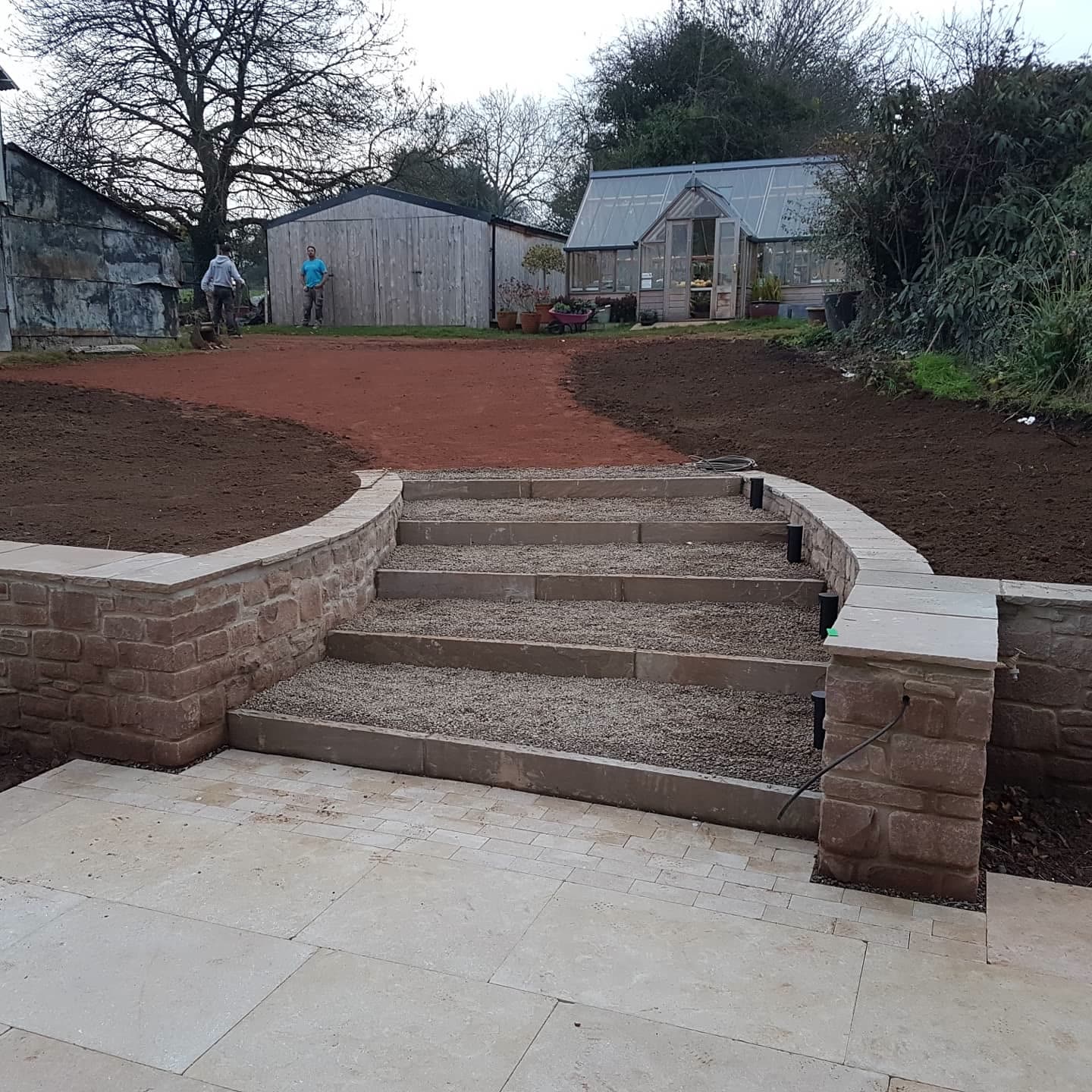 Sandstone steps and curved wall descending to a pale travertine paved patio