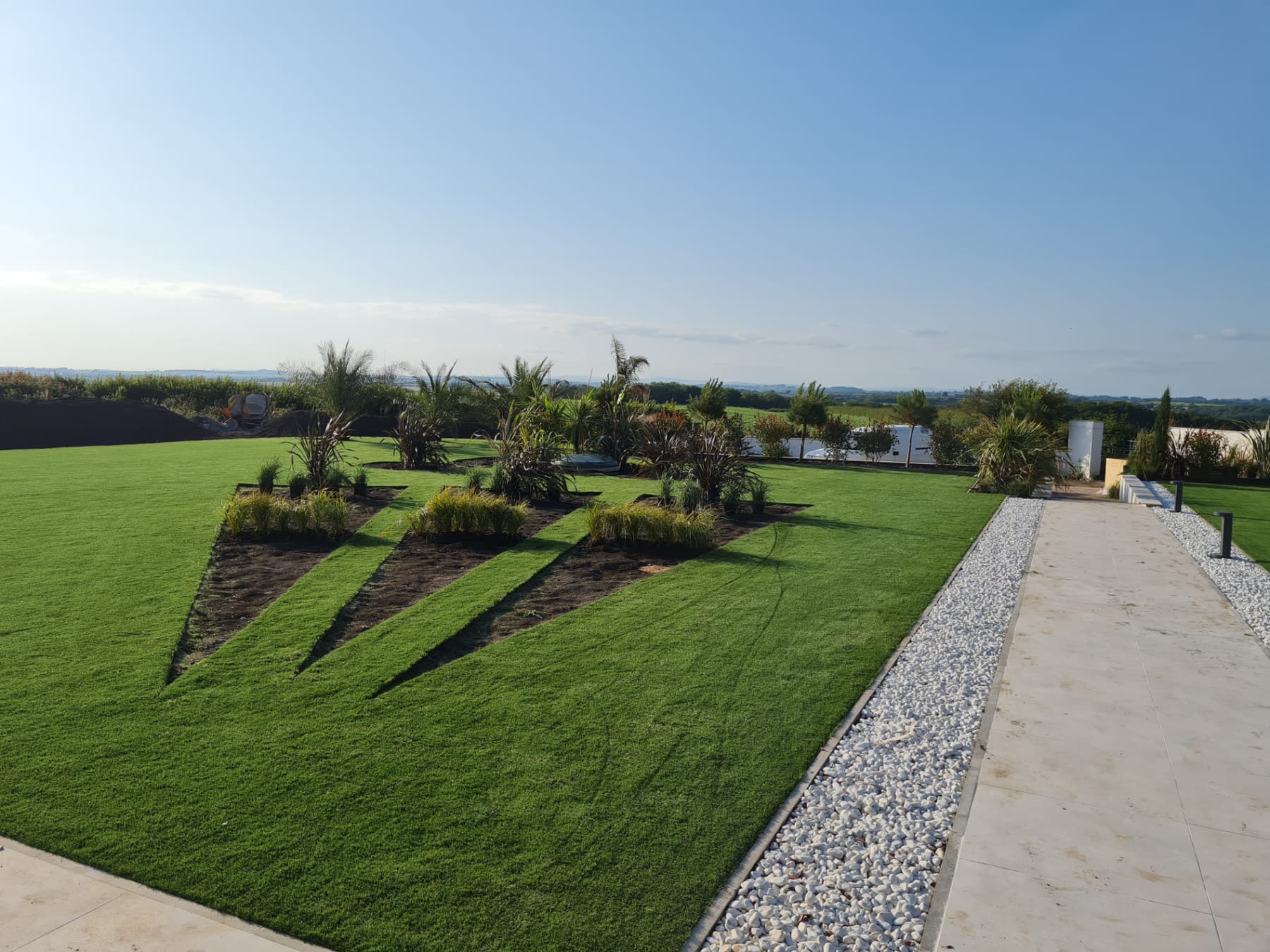 Large newly laid lawn with geometric planting beds, gravel borders and a paved path