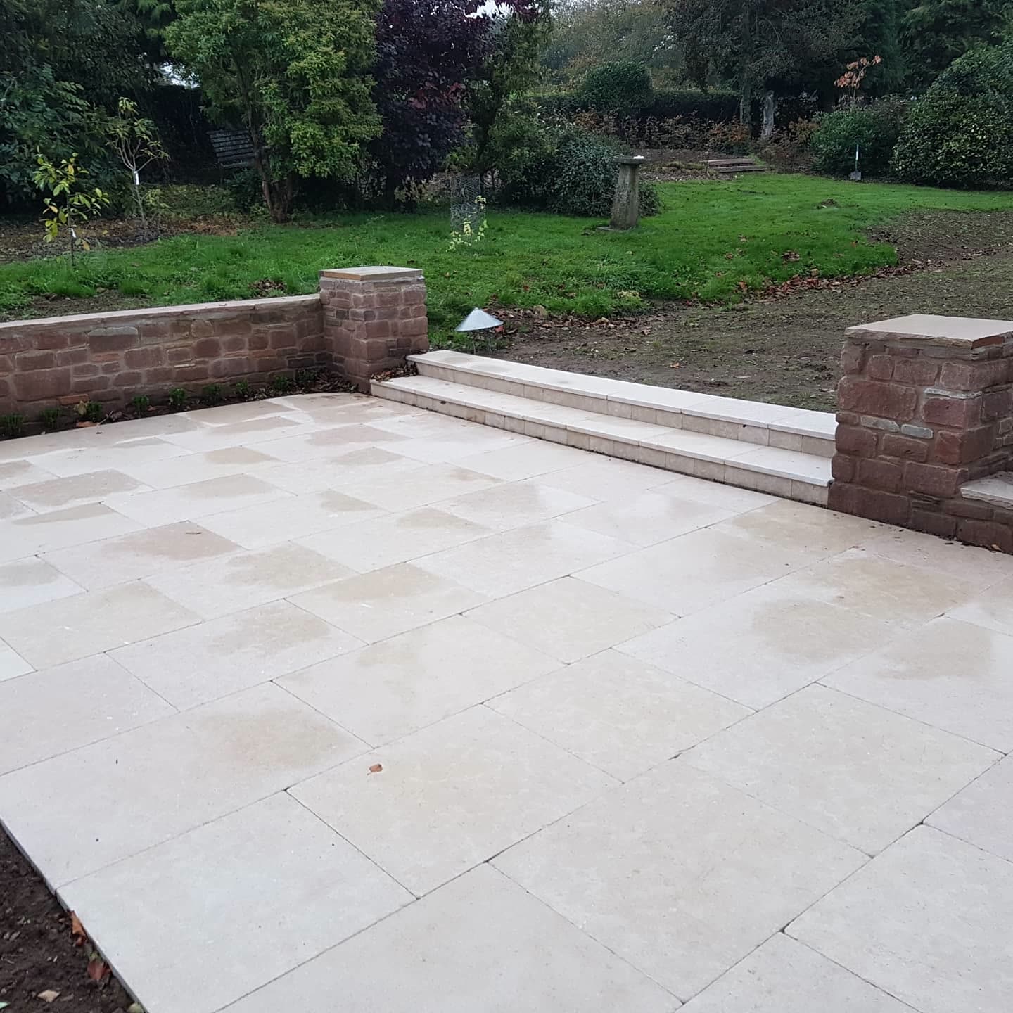 Cream travertine patio bordered by a red sandstone wall and steps leading to a lawn