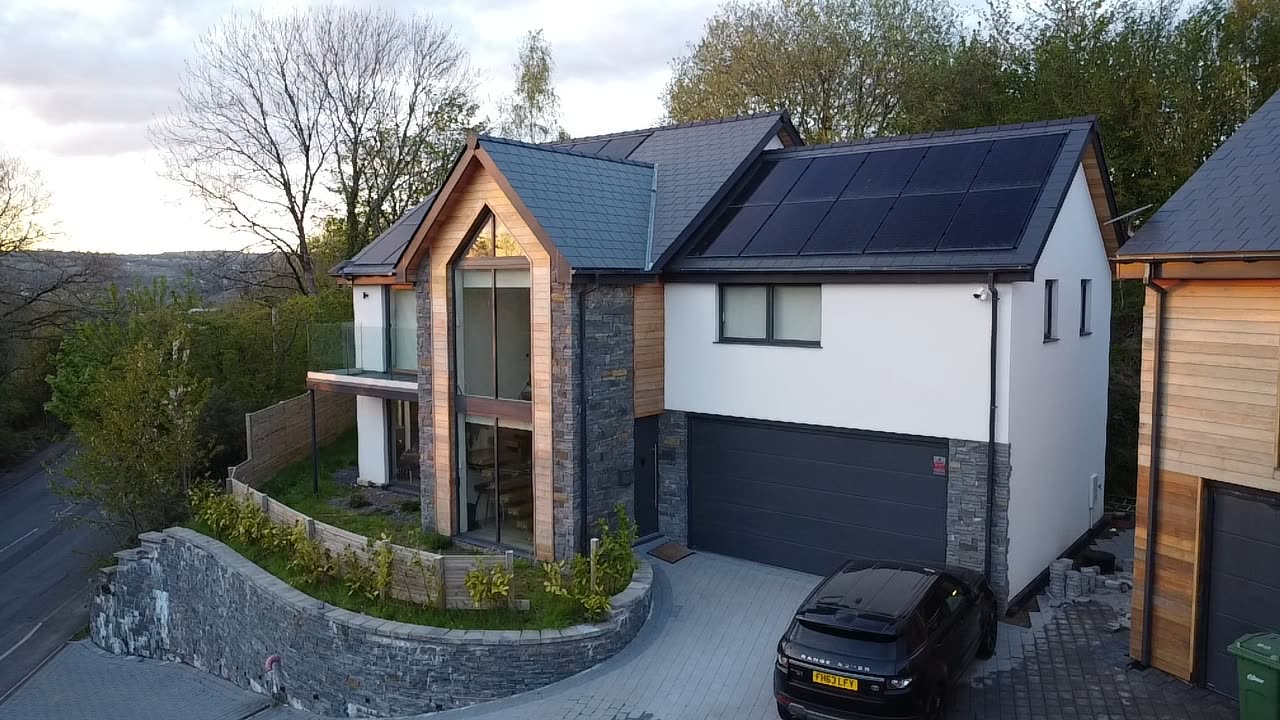 Aerial dusk view of a modern gabled home with timber and stone cladding and in-roof solar panels