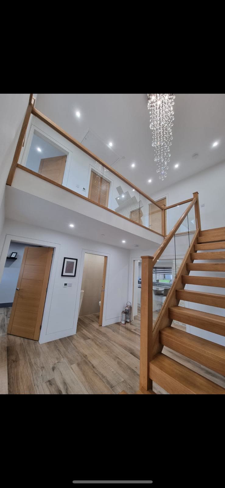 Double-height hallway with oak and glass staircase, galleried landing and crystal chandelier
