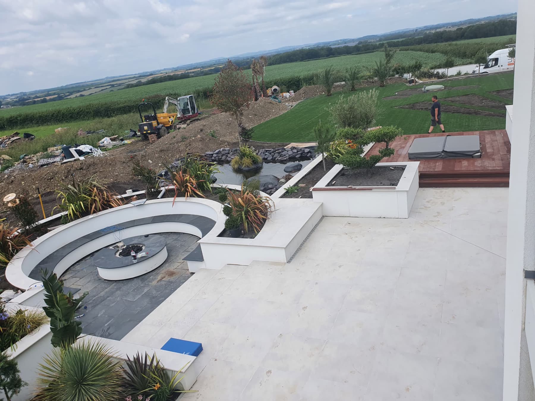 Aerial view of a landscaped garden with pond, fire pit seating and countryside beyond