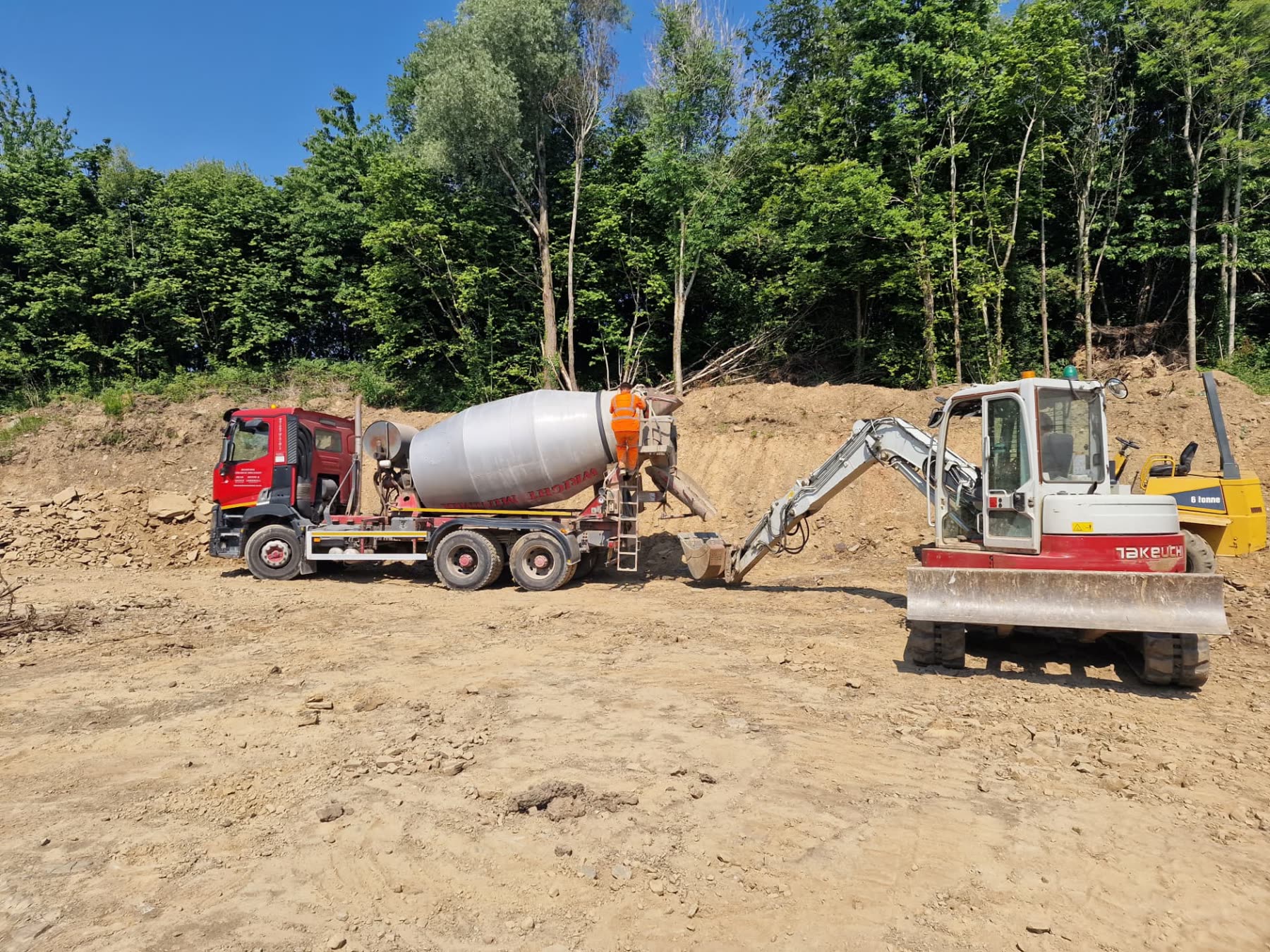 Concrete lorry and mini excavator working together on a muddy groundworks site