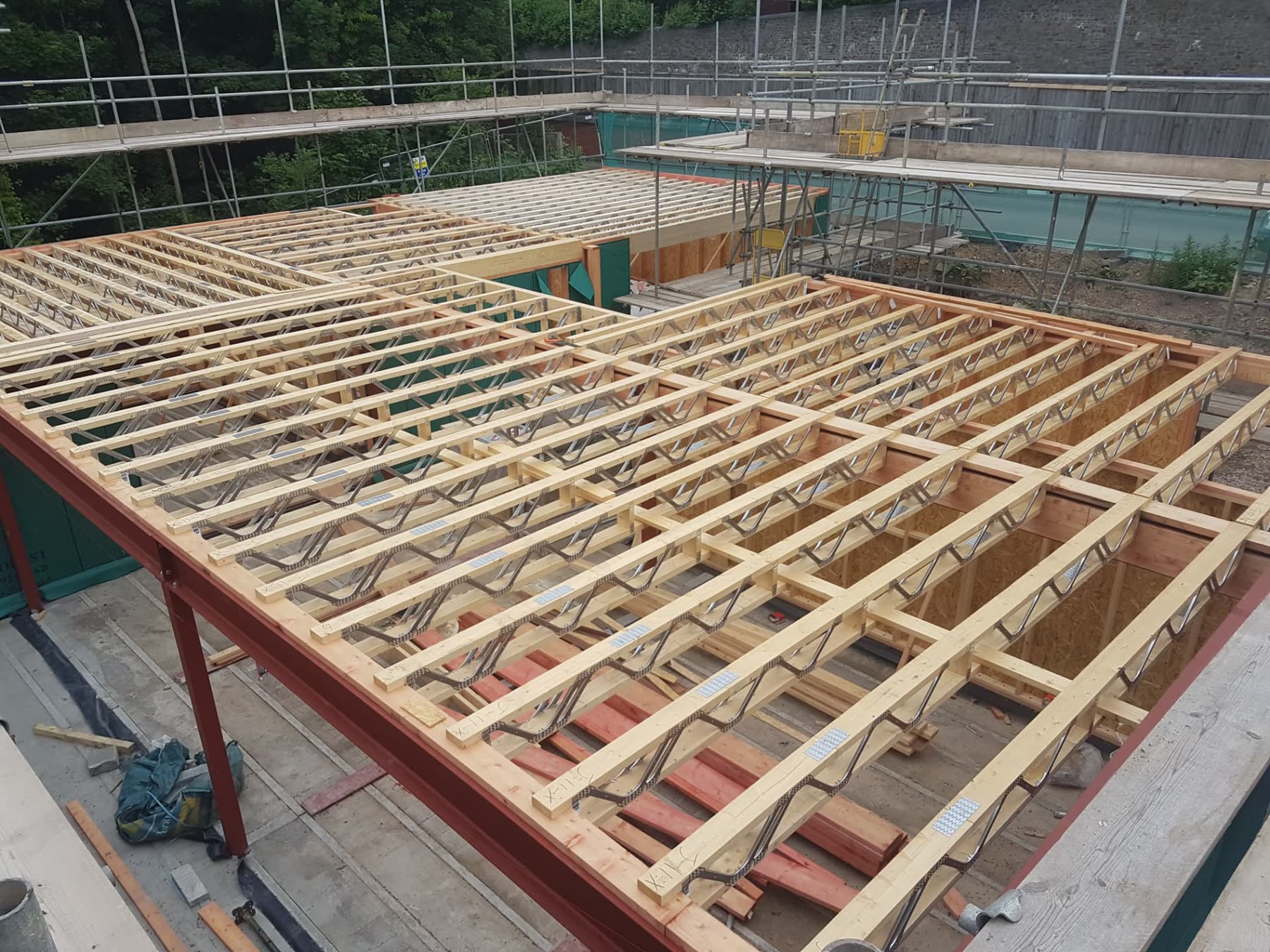 Engineered timber joists with metal web trusses fixed to a steel structural frame mid-build